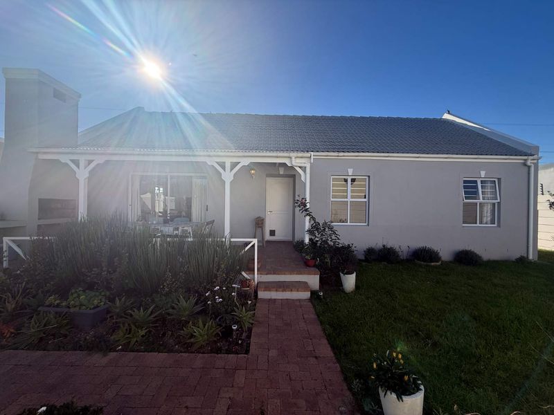 Rear view of the house featuring a covered patio, built-in braai, brick paved pathway, and a well-maintained garden area.