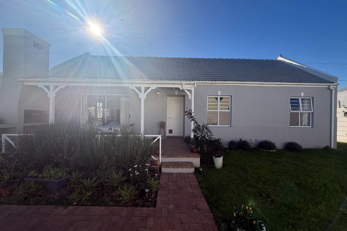 Rear view of the house featuring a covered patio, built-in braai, brick paved pathway, and a well-maintained garden area.