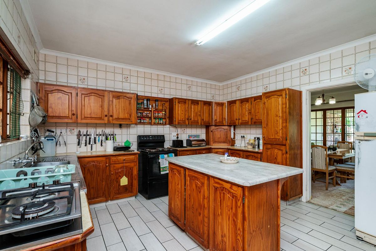 A traditional kitchen featuring wooden cabinetry, a central island with a laminate countertop, tiled walls, and a built-in stove and hob.