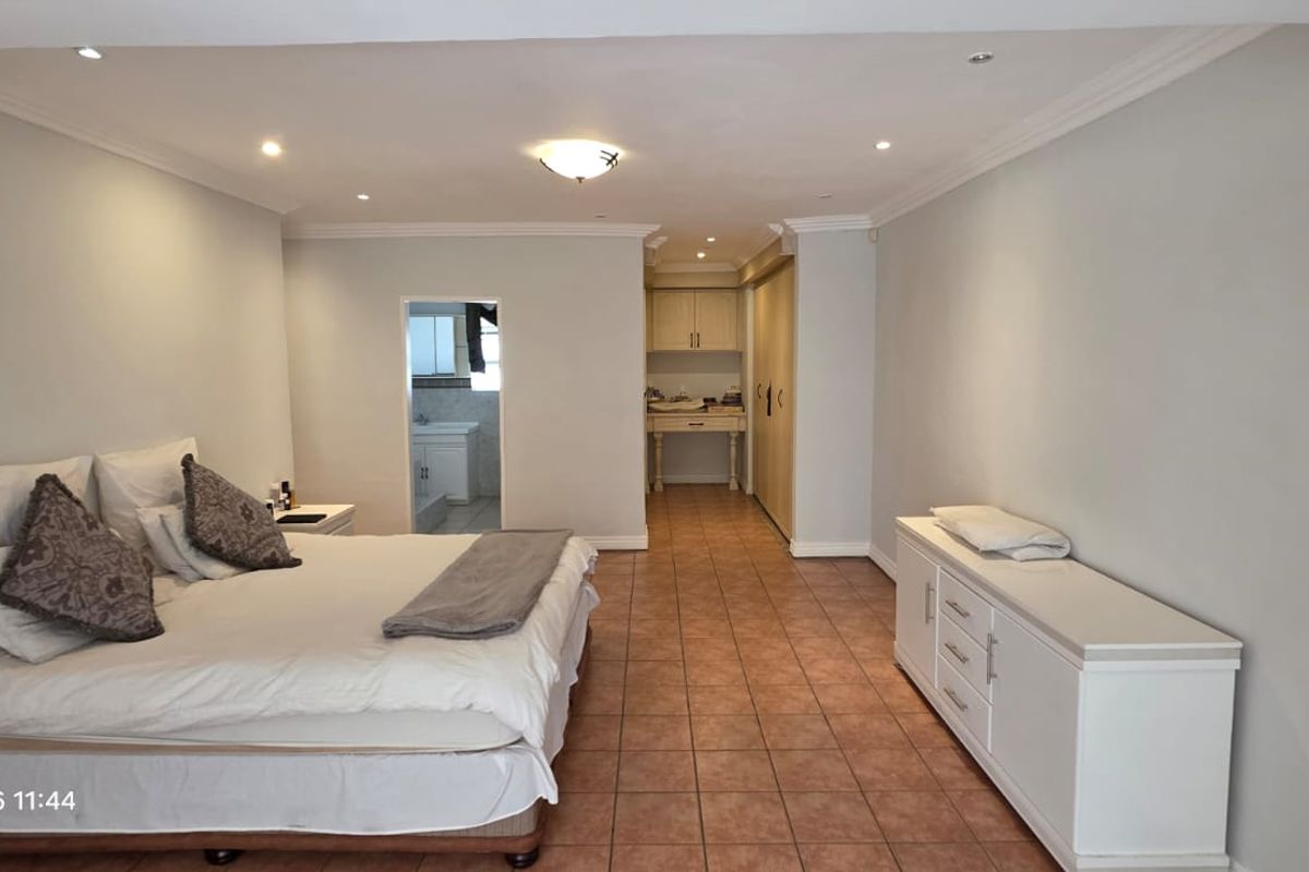 Spacious bedroom featuring tiled flooring, recessed lighting, ceiling coving, and built-in cupboards with direct access to an en-suite bathroom.