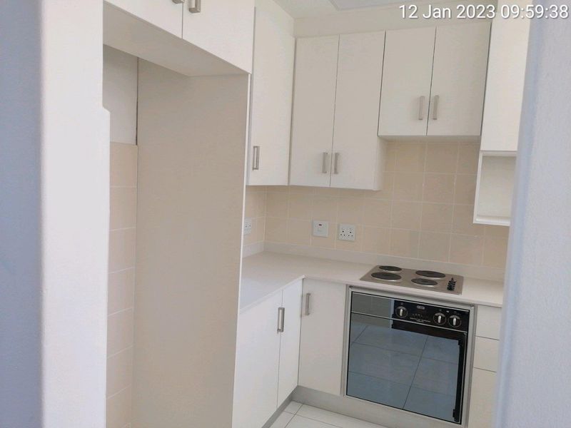 A clean, compact kitchen featuring white built-in cabinetry, a tiled backsplash, and integrated electric oven and hob.