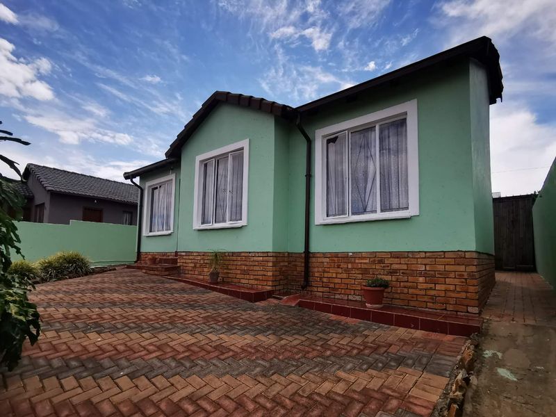 Front exterior view of a single-story house featuring a brick-paved driveway, brick base facade, and tiled roof.