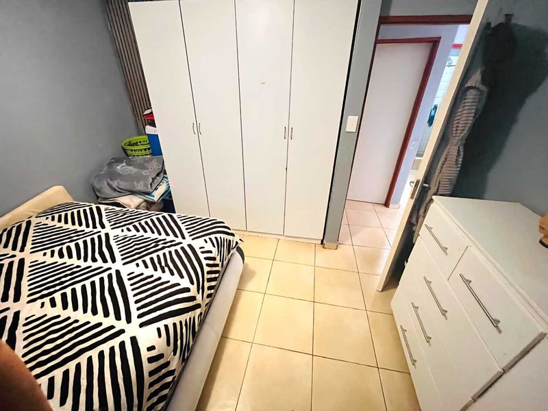 A bedroom featuring tiled flooring and a built-in wardrobe, with an adjacent doorway leading to another area of the apartment.