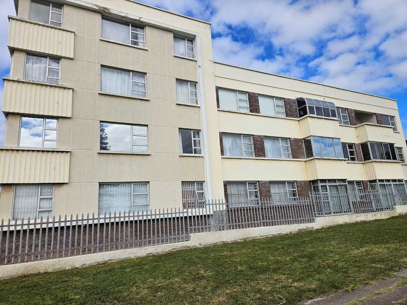 Exterior view of a multi-story apartment building featuring a cream facade, metal security fencing, and aluminium window frames.