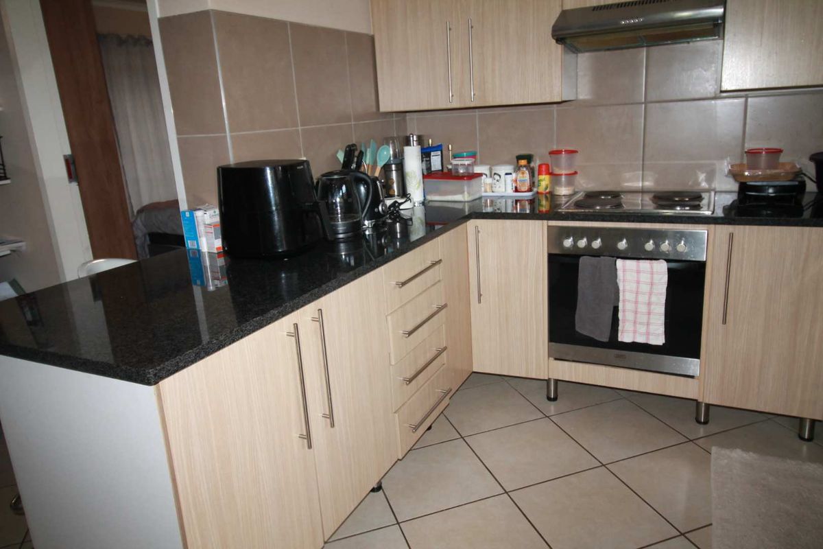 A functional kitchen featuring light wood-grain cabinetry, dark granite countertops, a built-in oven, electric hob, and stainless steel extractor fan with tiled splashbacks.