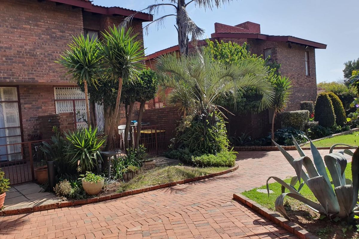 A view of the townhouse exterior featuring a brick facade, paved driveway, and established garden landscaping.