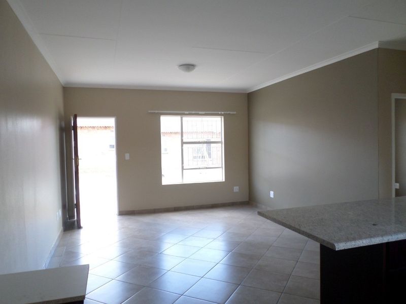 An open-plan living area featuring tiled flooring, a granite kitchen counter, and natural light through a window with security bars.