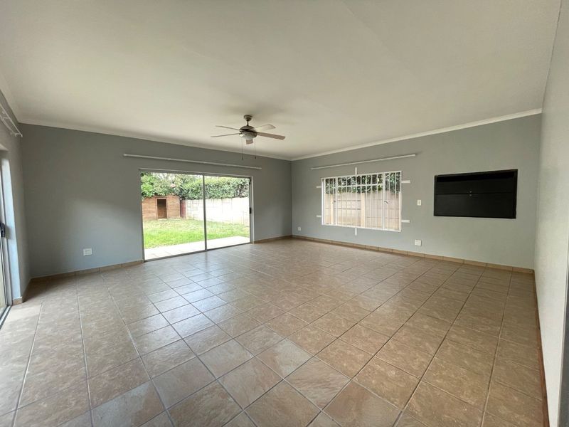 Spacious, empty living room featuring tiled flooring, a ceiling fan, and large sliding glass doors providing direct access to the rear garden.