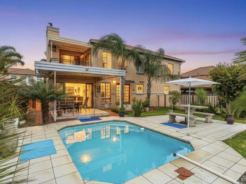Rear view of the house featuring a swimming pool, paved pool deck, covered patio area, and an upper-level balcony.
