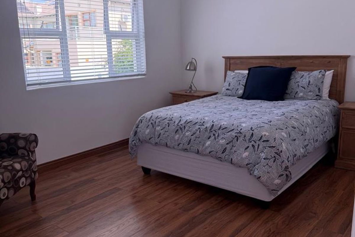 A well-maintained bedroom featuring warm-toned laminate flooring, recessed downlighting, and clean white walls with decorative cove cornicing.