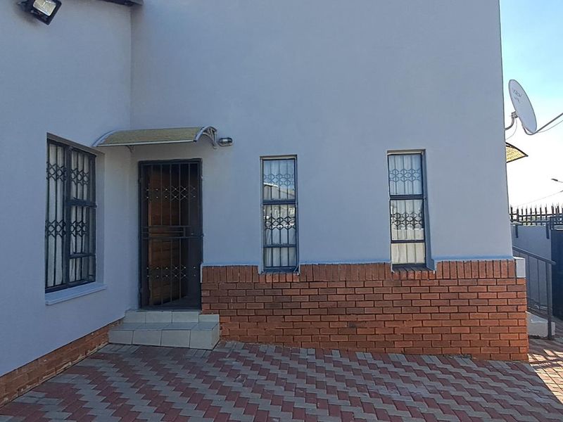 Front exterior view of the house featuring a paved driveway, brick facade detailing, security gates, and window burglar bars.