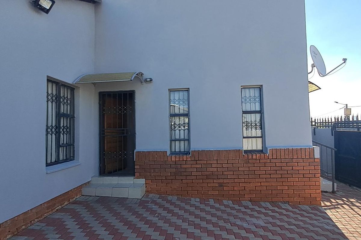 Front exterior view of the house featuring a paved driveway, brick facade detailing, security gates, and window burglar bars.