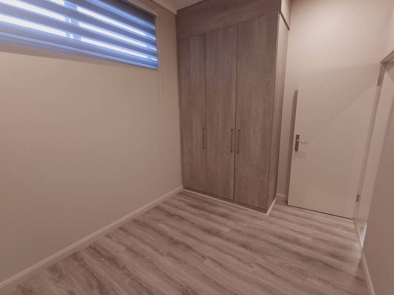 A clean, modern bedroom featuring light wood-look laminate flooring, built-in cupboards, and a roller blind on the window.