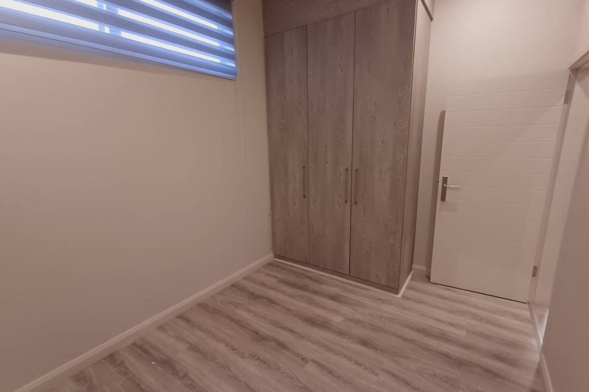 A clean, modern bedroom featuring light wood-look laminate flooring, built-in cupboards, and a roller blind on the window.