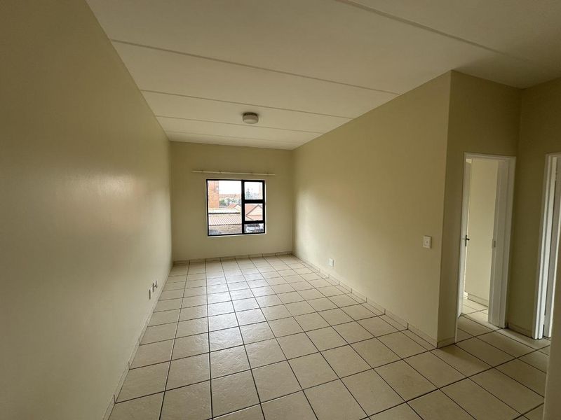 A bright, empty living area featuring neutral wall tones, tiled flooring, and a large window providing natural light.
