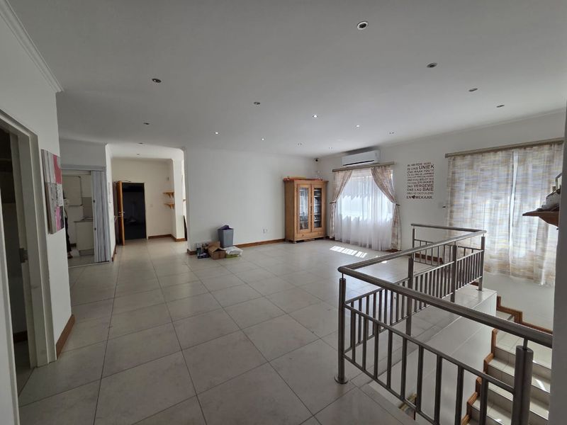 Spacious open-plan living area featuring tiled flooring, recessed downlighting, a split-system air conditioner, and a stainless steel balustrade overlooking the staircase.