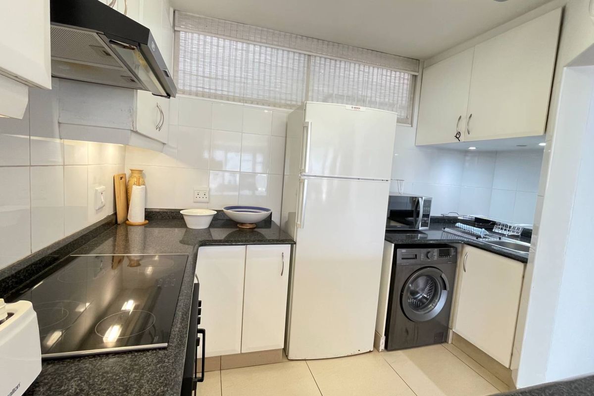 Functional kitchen featuring dark granite countertops, white cabinetry, tiled backsplash, and integrated appliances including an electric hob and extractor fan.
