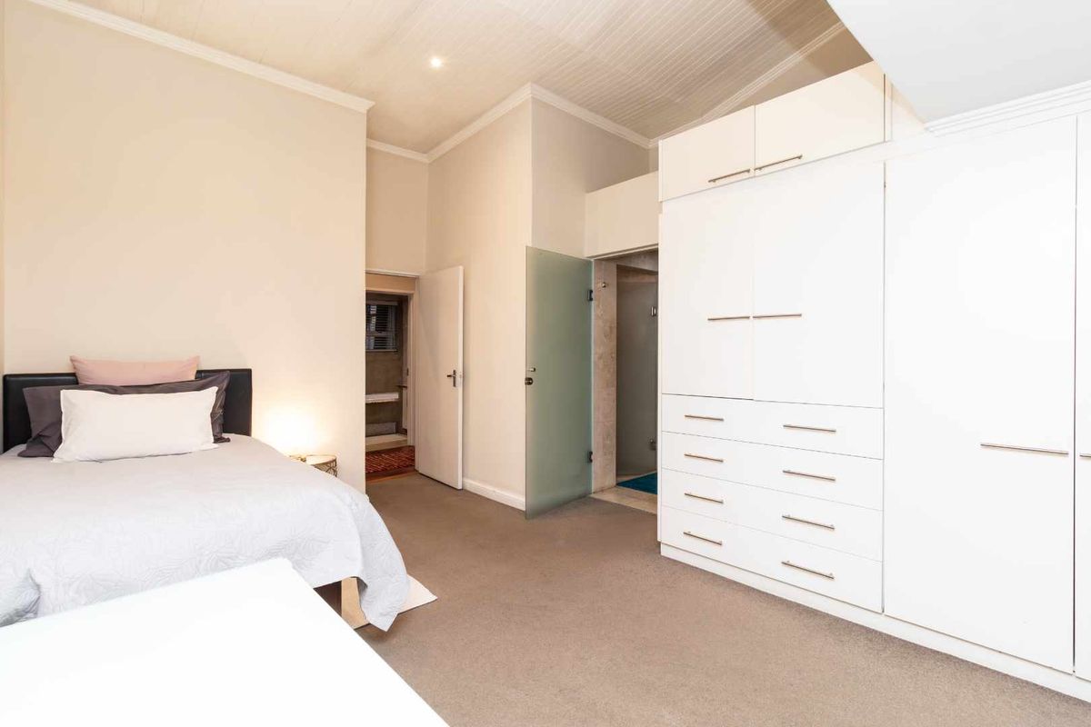 Spacious bedroom featuring built-in floor-to-ceiling cabinetry, neutral carpeting, and an en-suite bathroom with a frosted glass door.