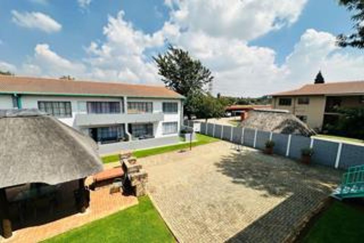 Exterior view of the apartment complex featuring a communal courtyard, paved area, and a thatched lapa structure.