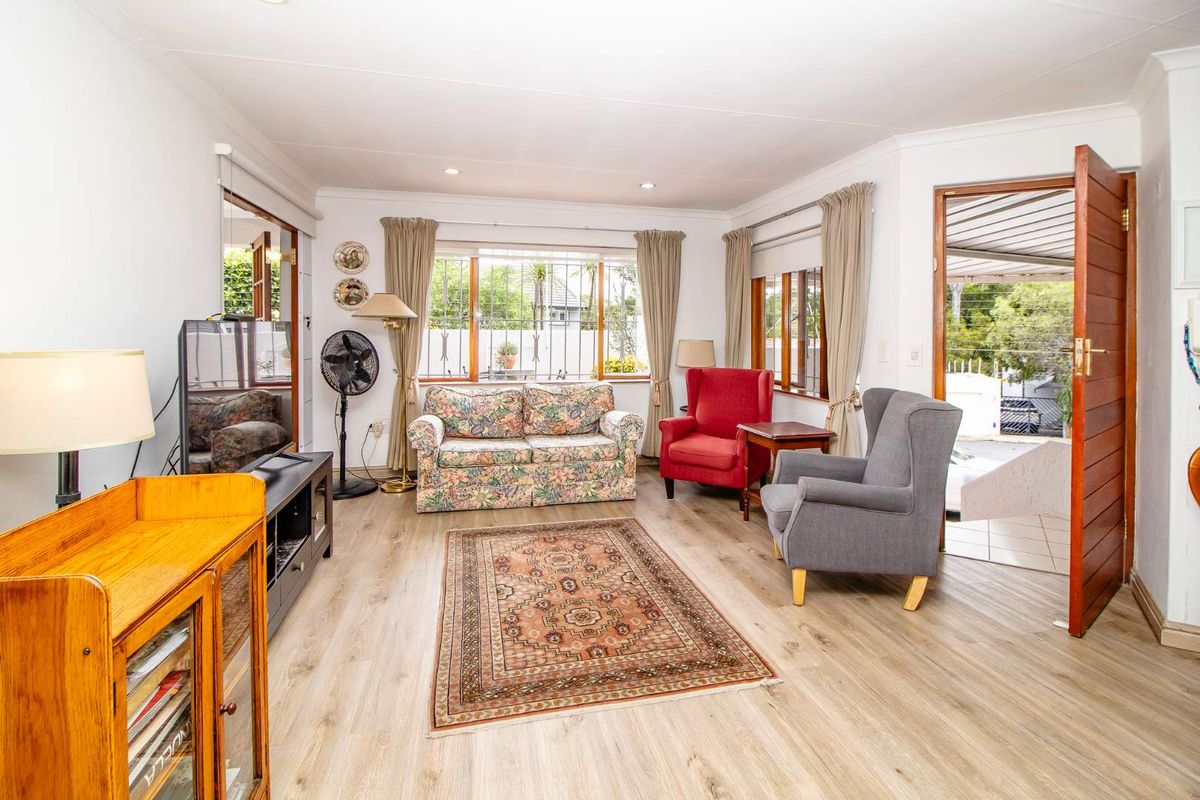 A bright living room featuring light wood-look flooring, recessed ceiling lighting, and large windows with security bars, providing access to an outdoor patio area.