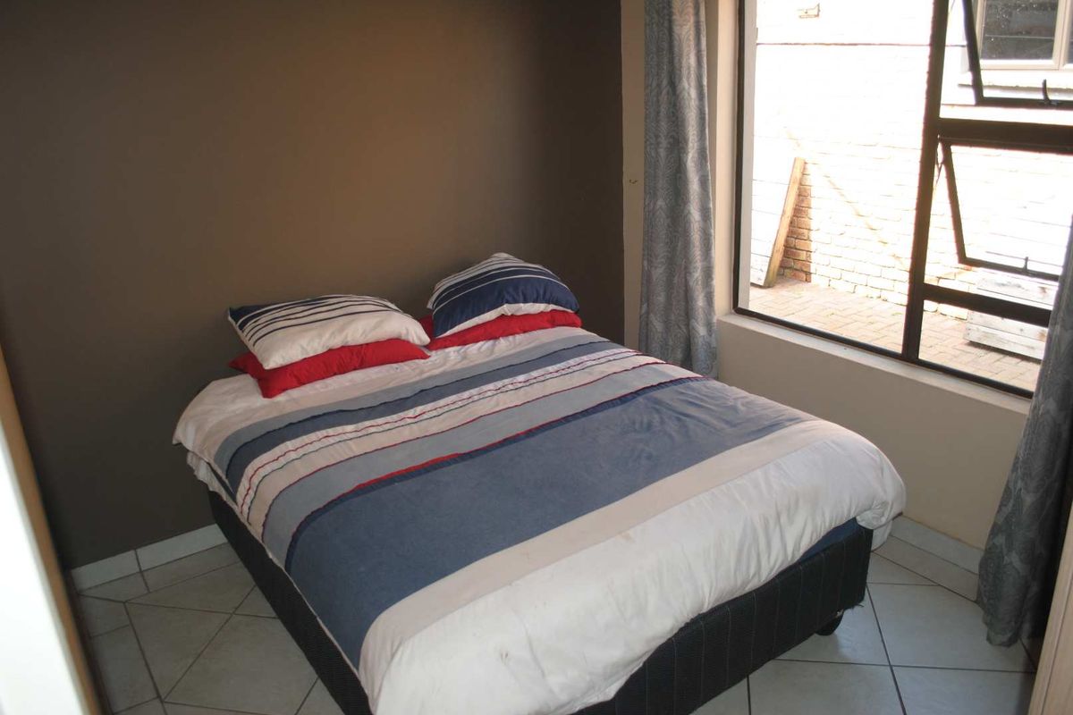 A bedroom featuring tiled flooring and a large window providing natural light, with a neutral wall finish.