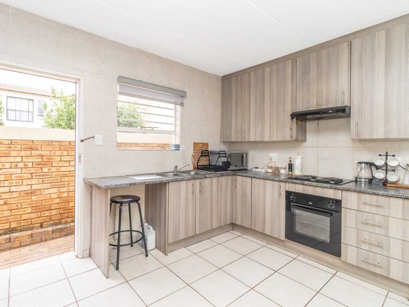 Functional kitchen featuring wood-look cabinetry, built-in oven and hob, tiled splashbacks, and direct access to a private rear courtyard area.