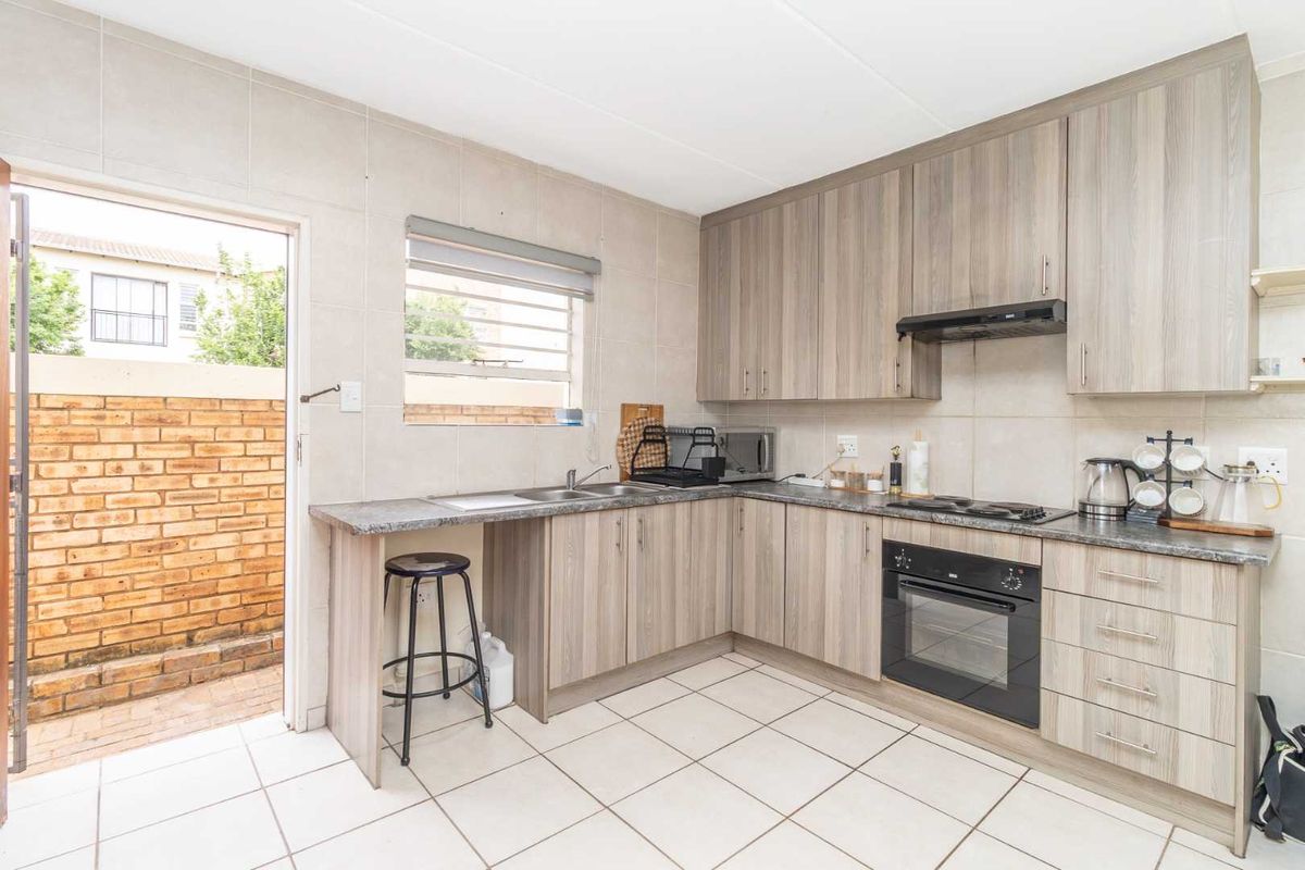 Functional kitchen featuring wood-look cabinetry, built-in oven and hob, tiled splashbacks, and direct access to a private rear courtyard area.