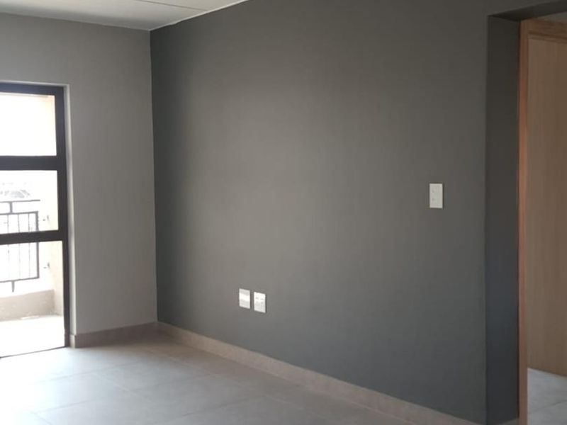 A bright, empty living area featuring modern grey tiled flooring, neutral painted walls, and an aluminium window frame leading to an outdoor space.