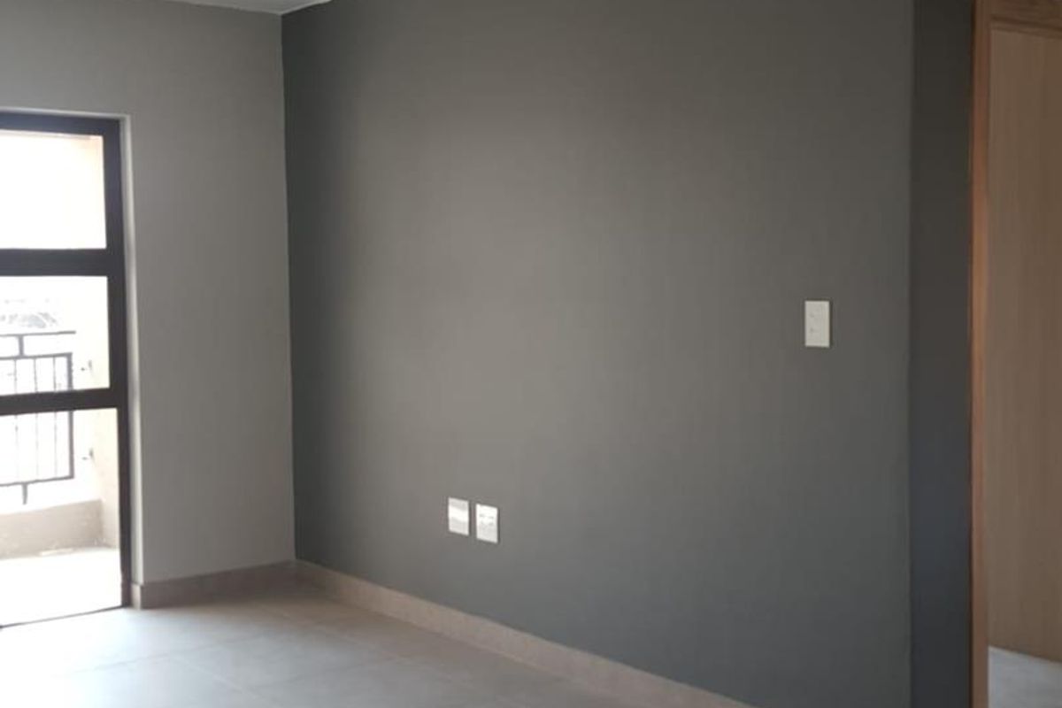 A bright, empty living area featuring modern grey tiled flooring, neutral painted walls, and an aluminium window frame leading to an outdoor space.