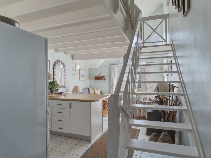 Open plan living area featuring a white staircase, kitchen island with wooden countertop, tiled flooring, and exposed ceiling beams.