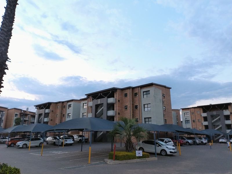 Exterior view of a multi-story brick apartment complex featuring covered parking bays and paved driveway access.