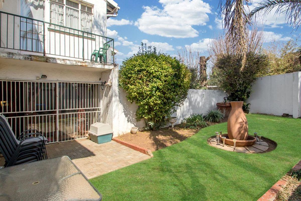 A private rear garden featuring a paved patio area, lawn, and a decorative water feature, overlooked by an upper-level balcony.