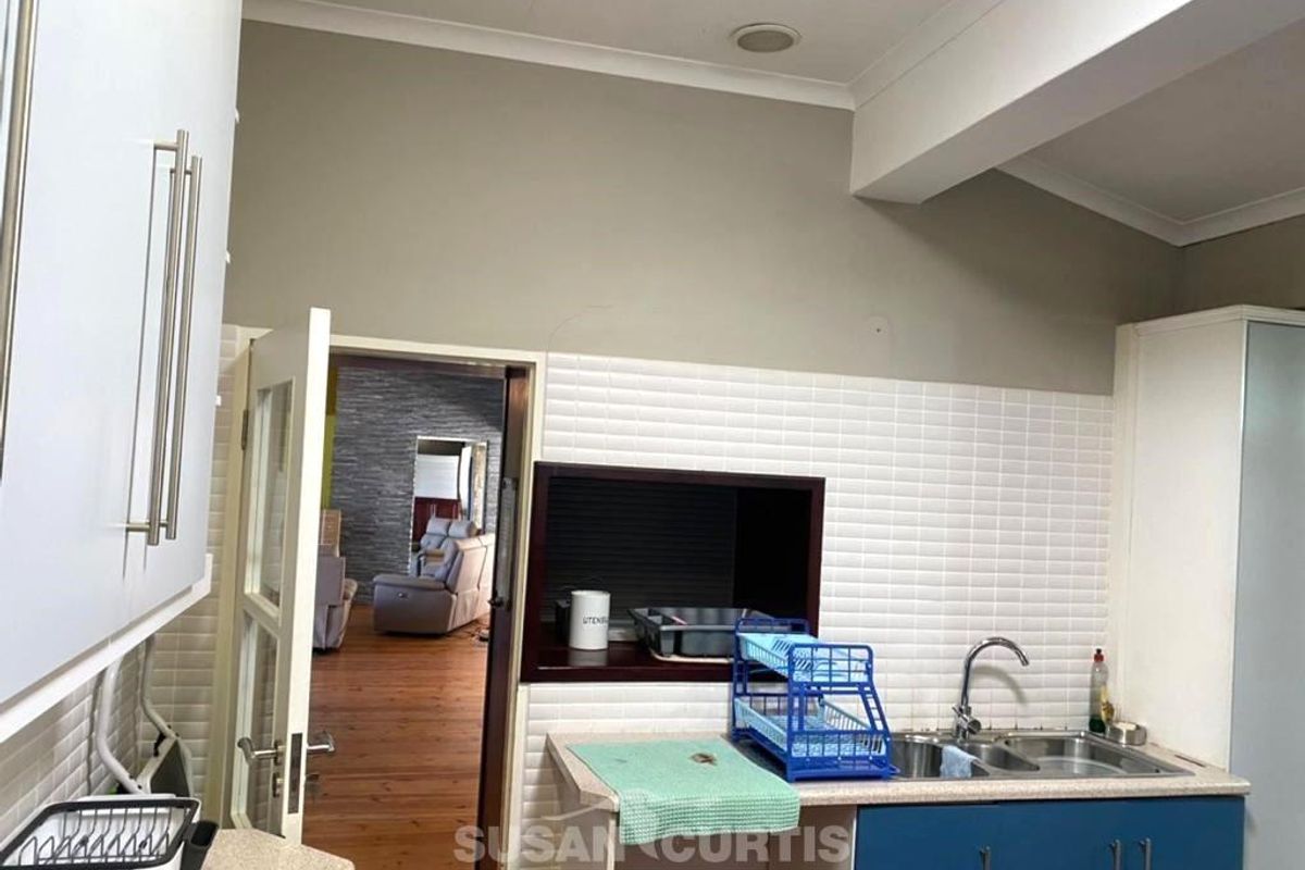 A functional kitchen area featuring a double sink, tiled splashback, and built-in cabinetry, with a doorway leading to an adjacent living space.