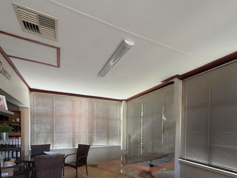 A functional office space featuring tiled flooring, integrated air conditioning, and large windows fitted with venetian blinds for natural light control.