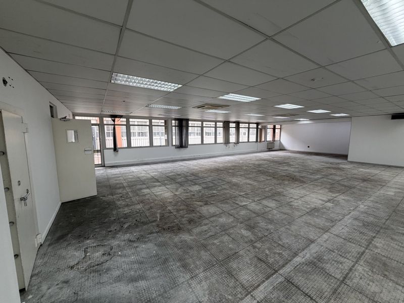 Spacious open-plan industrial office area featuring a suspended ceiling with recessed lighting and large windows providing ample natural light.