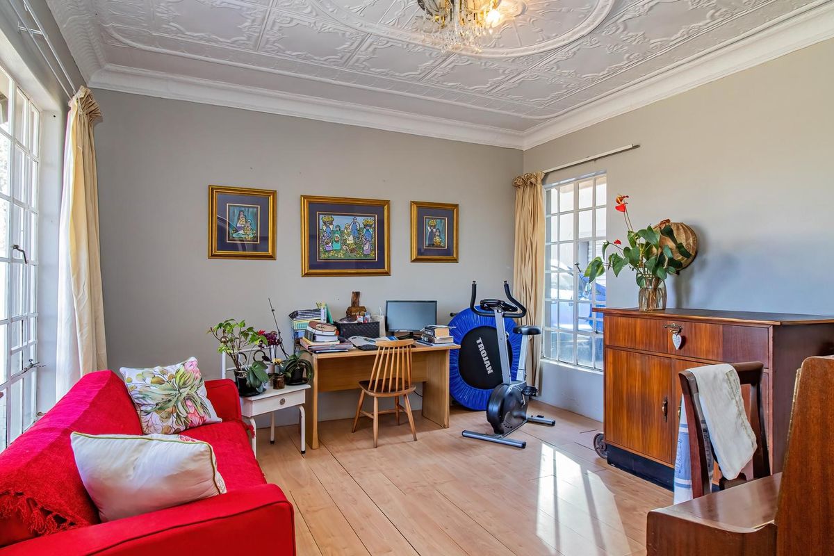A bright living room featuring classic wooden flooring and an ornate pressed metal ceiling, offering a characterful space with ample natural light.