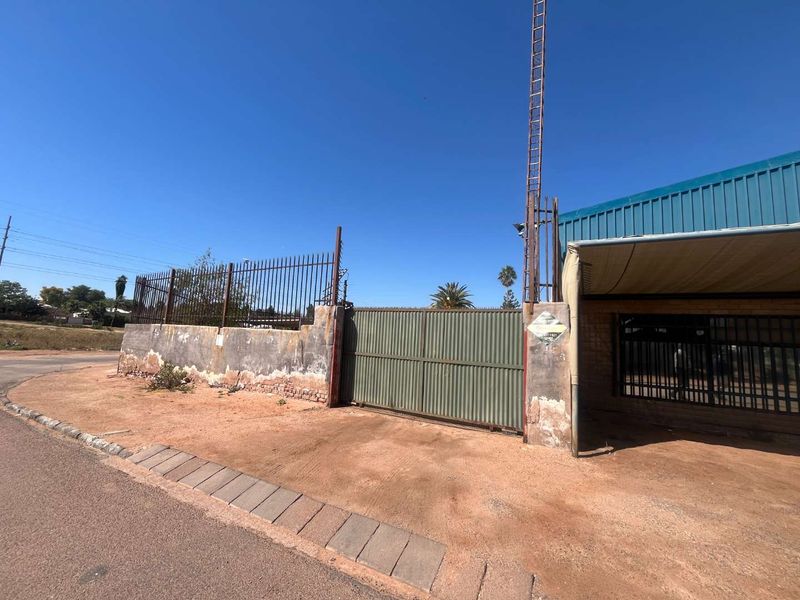 Front exterior view of the property featuring a metal security gate, perimeter wall with fencing, and a metal roof structure.