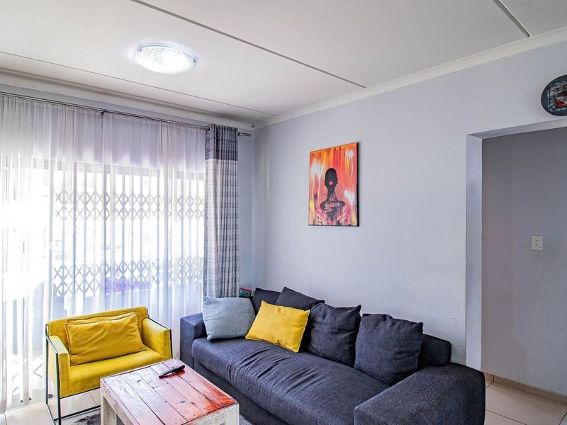 A bright living room featuring tiled flooring, a sliding glass door with a security gate, and direct access to an adjacent bathroom area.