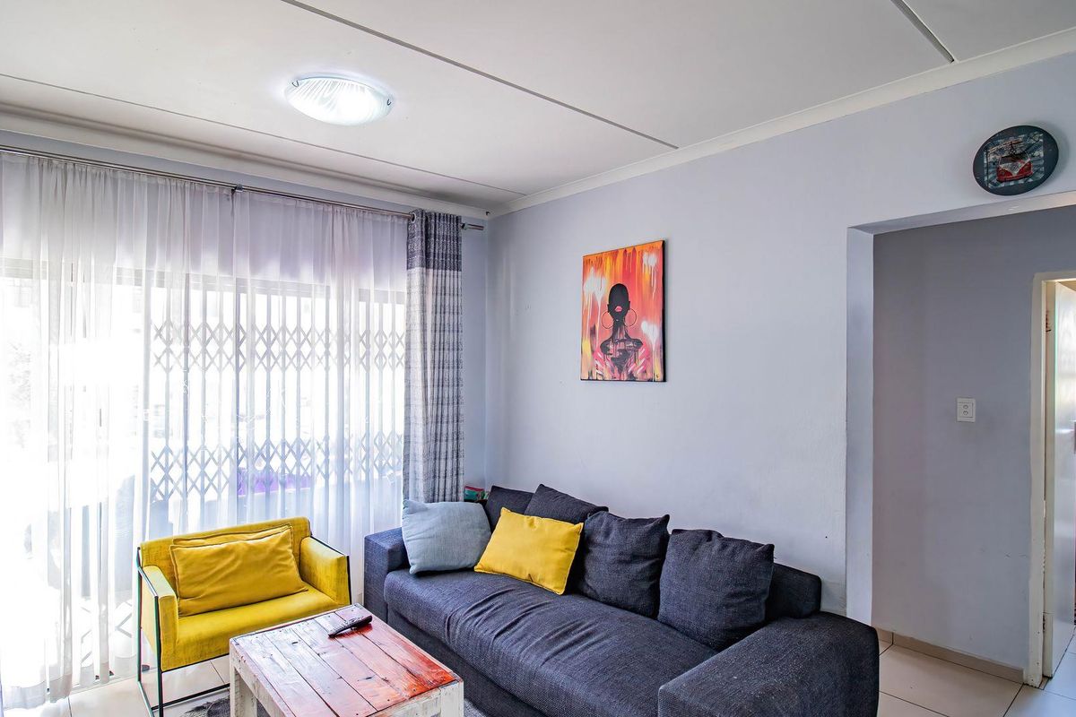 A bright living room featuring tiled flooring, a sliding glass door with a security gate, and direct access to an adjacent bathroom area.