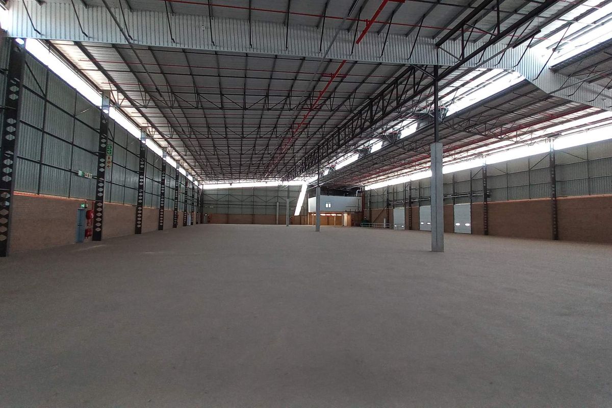 Expansive industrial warehouse space featuring high ceilings with exposed steel trusses, concrete flooring, and multiple roller shutter doors for efficient logistics and storage operations.