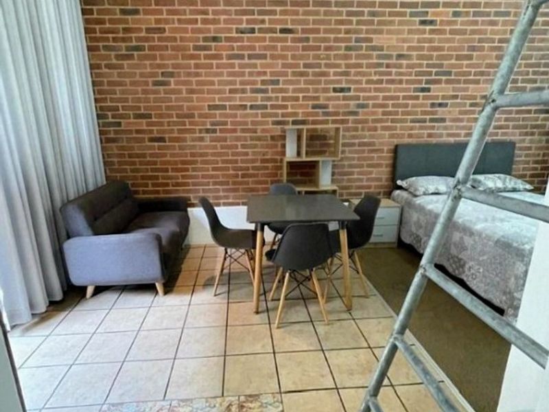 Open-plan living area featuring an exposed brick feature wall and ceramic tiled flooring, currently configured as a combined living and sleeping space.