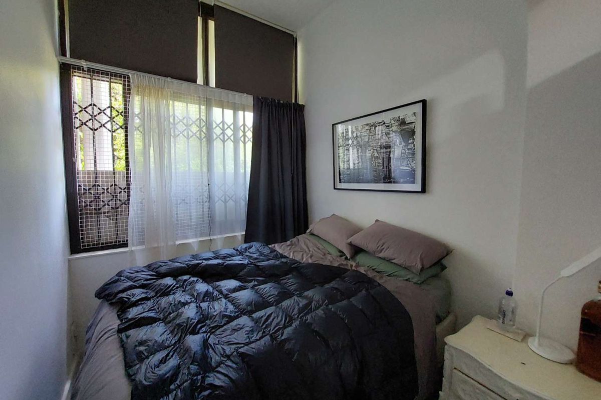 A compact bedroom featuring a window with integrated security gate and roller blinds, providing a functional and private sleeping space.