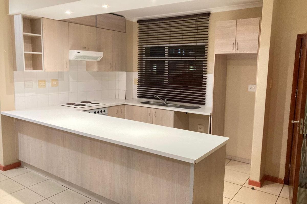 A functional kitchen featuring light wood cabinetry, a breakfast bar, built-in electric stove, and tiled flooring with a window overlooking the exterior.