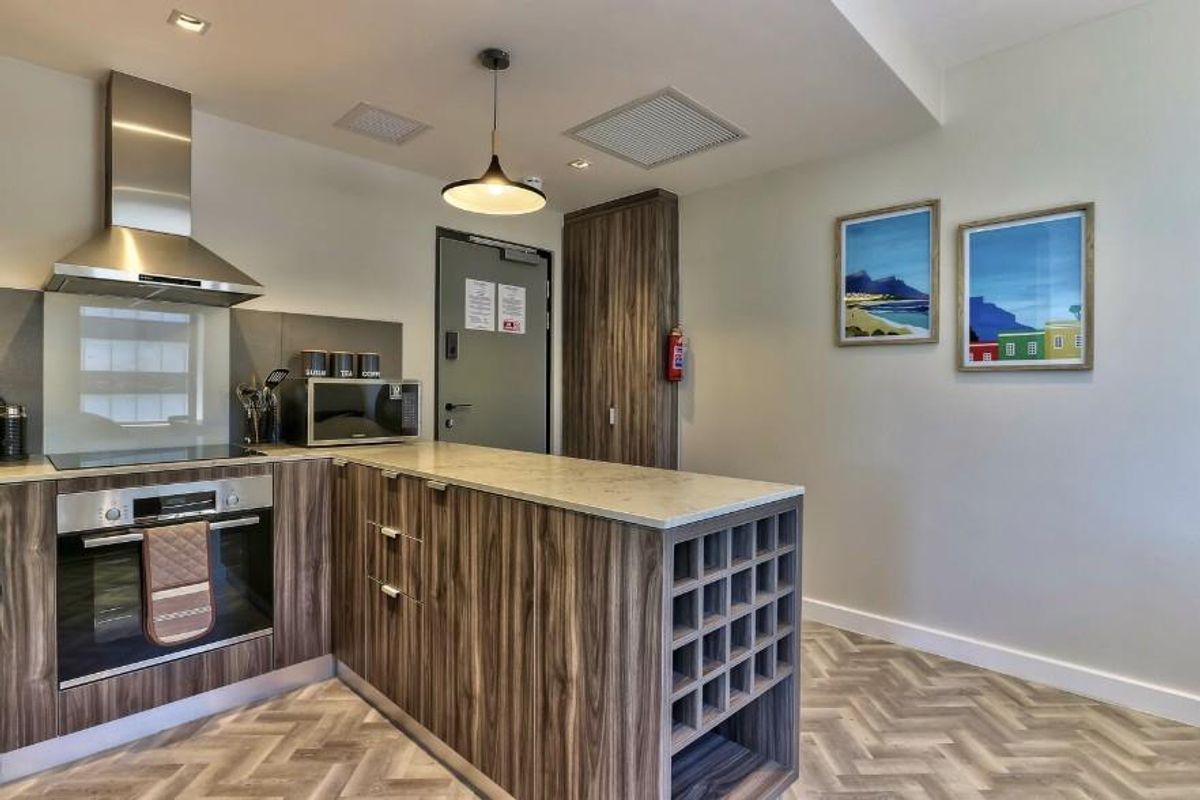 Modern kitchen featuring wood-grain cabinetry, stone countertops, built-in oven, stainless steel extractor fan, and integrated wine rack storage.
