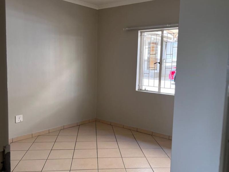 A clean, empty bedroom featuring neutral wall paint, tiled flooring, and a window fitted with security bars.