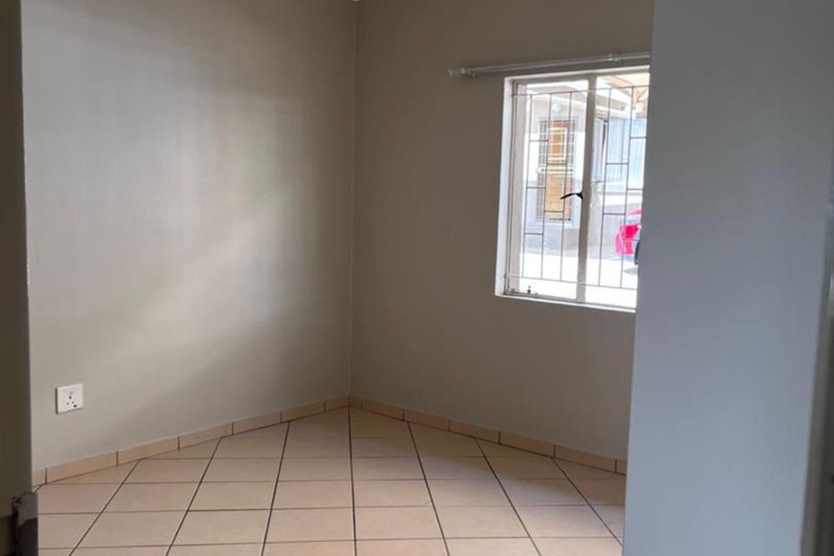 A clean, empty bedroom featuring neutral wall paint, tiled flooring, and a window fitted with security bars.