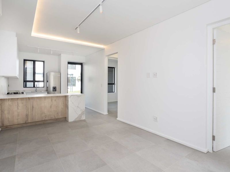 Modern open-plan living area featuring a sleek kitchen with stone countertops, gas hob, recessed lighting, and neutral tiled flooring throughout.