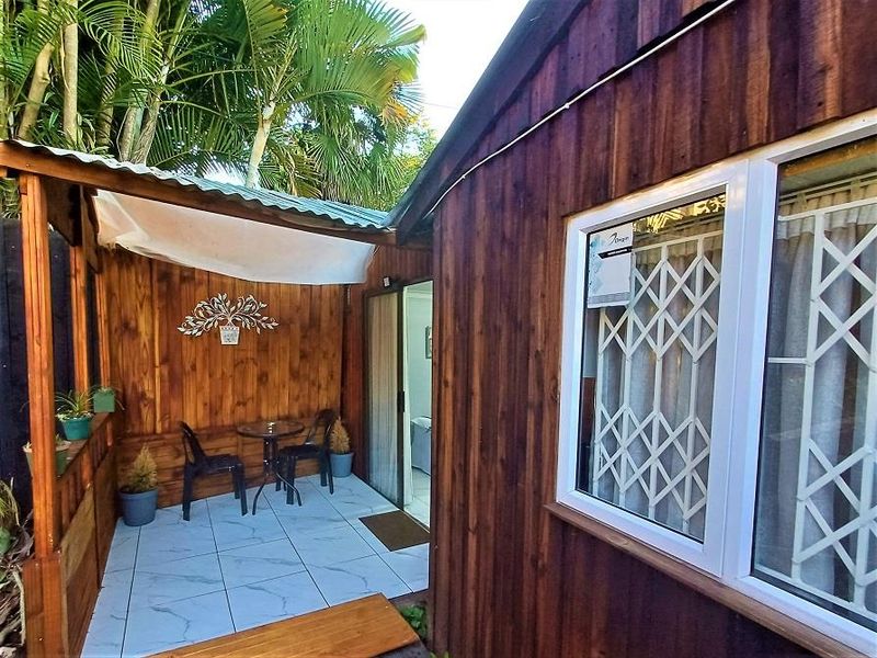 A covered outdoor patio area featuring timber wall cladding, tiled flooring, and a sliding door entrance to the cottage interior.