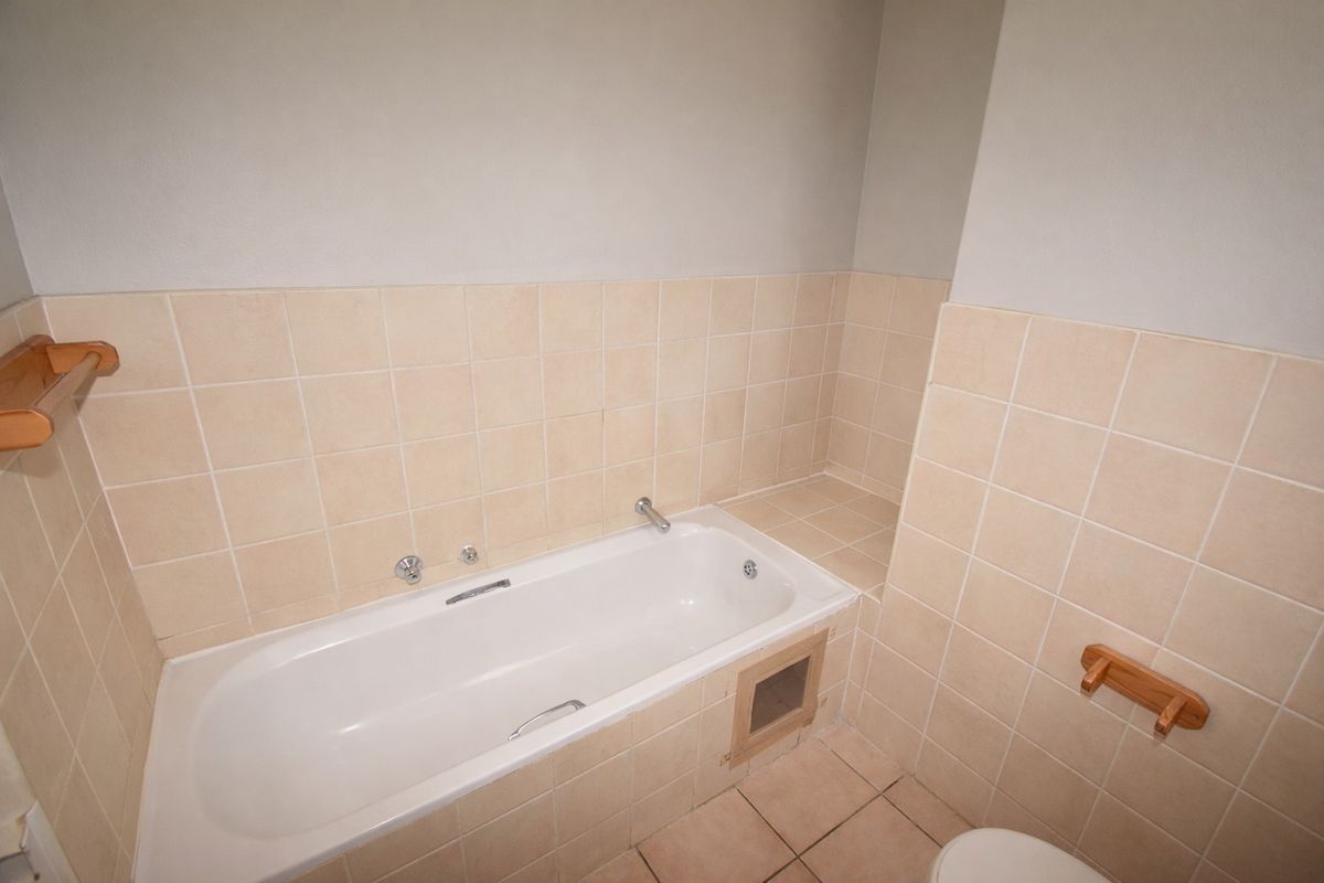 A functional bathroom featuring a built-in bathtub with ceramic wall and floor tiling, offering a neutral base for potential cosmetic updates.