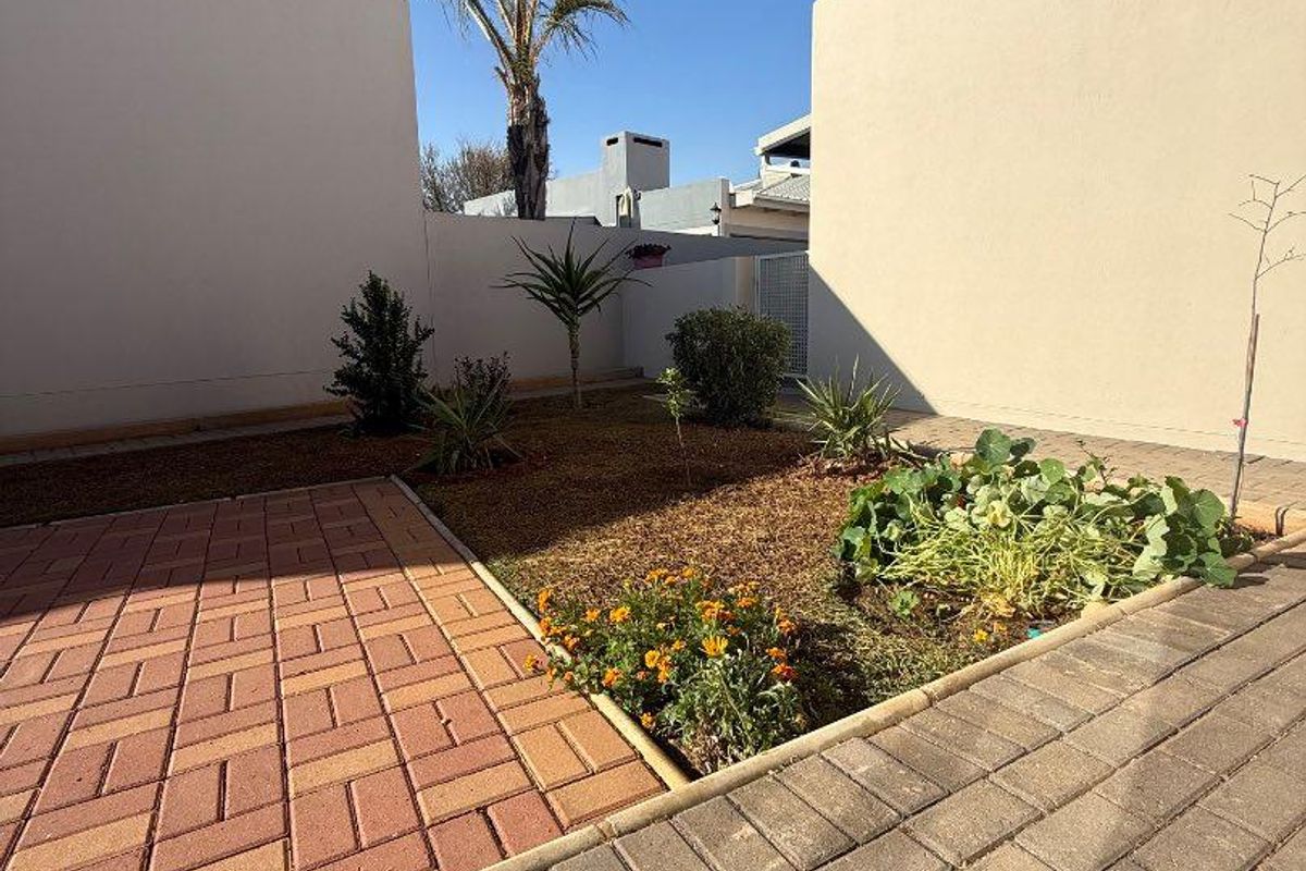 A private rear courtyard featuring paved walkways and a landscaped garden area enclosed by high boundary walls.